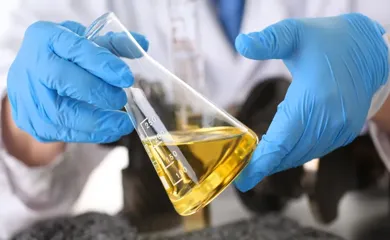 hands wearing blue gloves holding a glass test tube filled with fluid